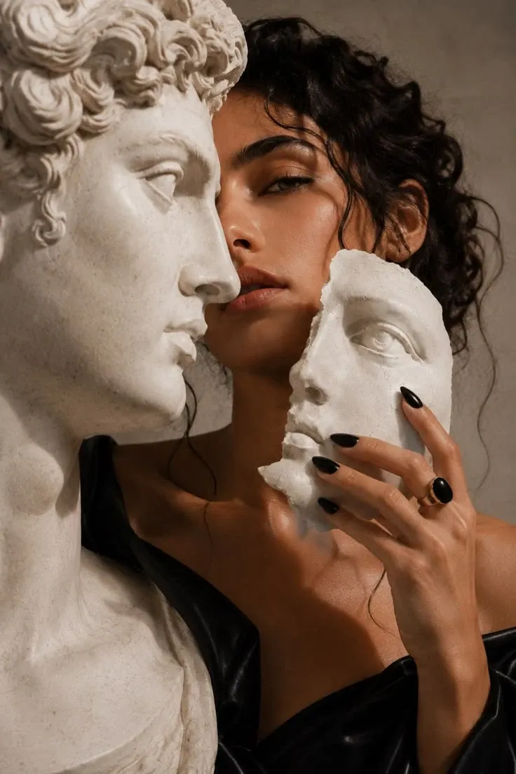 Mujer sosteniendo fragmentos de un rostro escultórico junto a un busto de mármol.